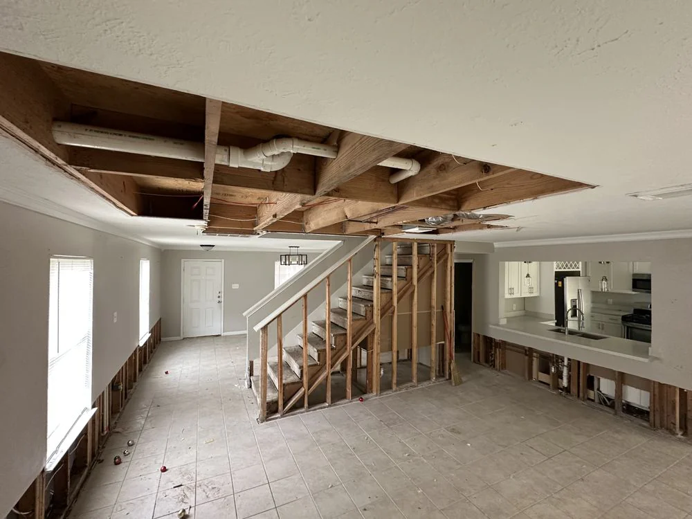 Interior with stairs and kitchen visible, ceiling joists exposed and drywall flood-cut at the baseboards after Bayou City water damage demo